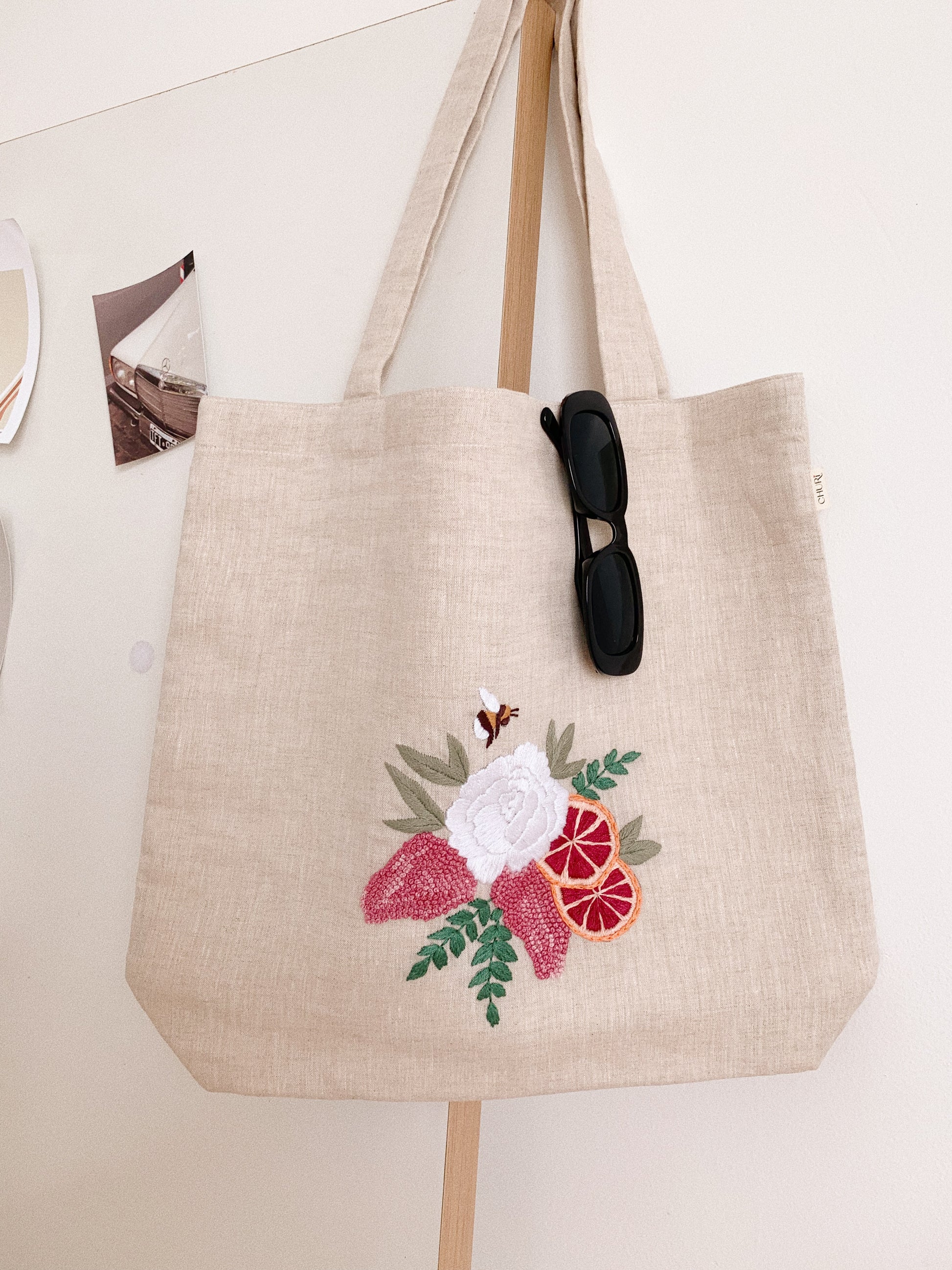 Hand embroidered linen tote bag with bee above a flower embroidery.