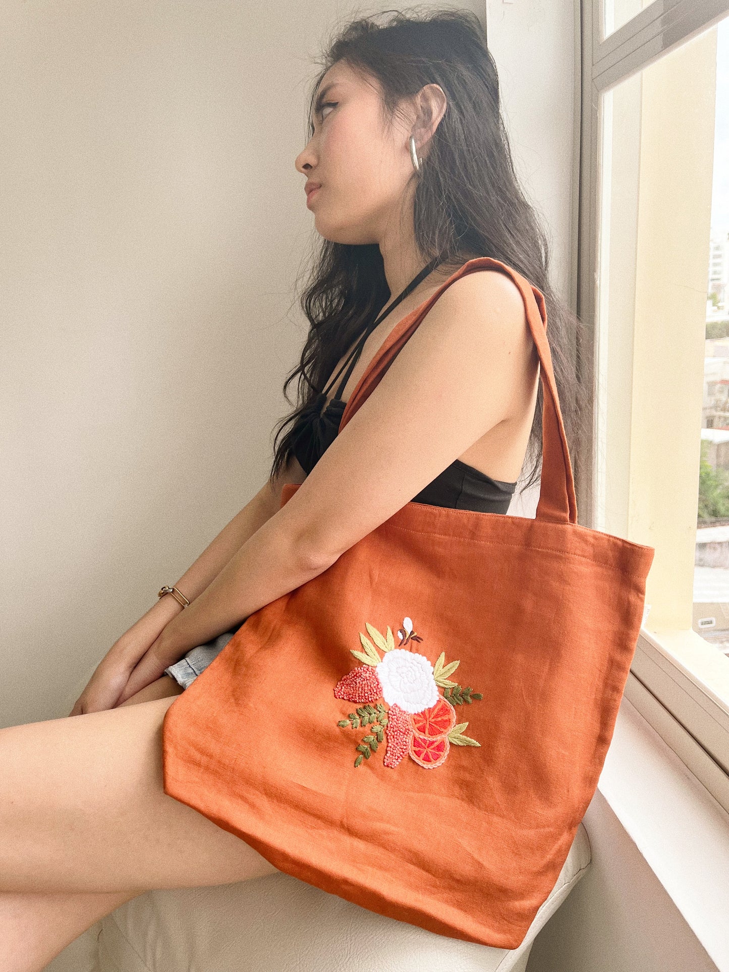 Hand embroidered linen tote bag with bee above a flower embroidery.