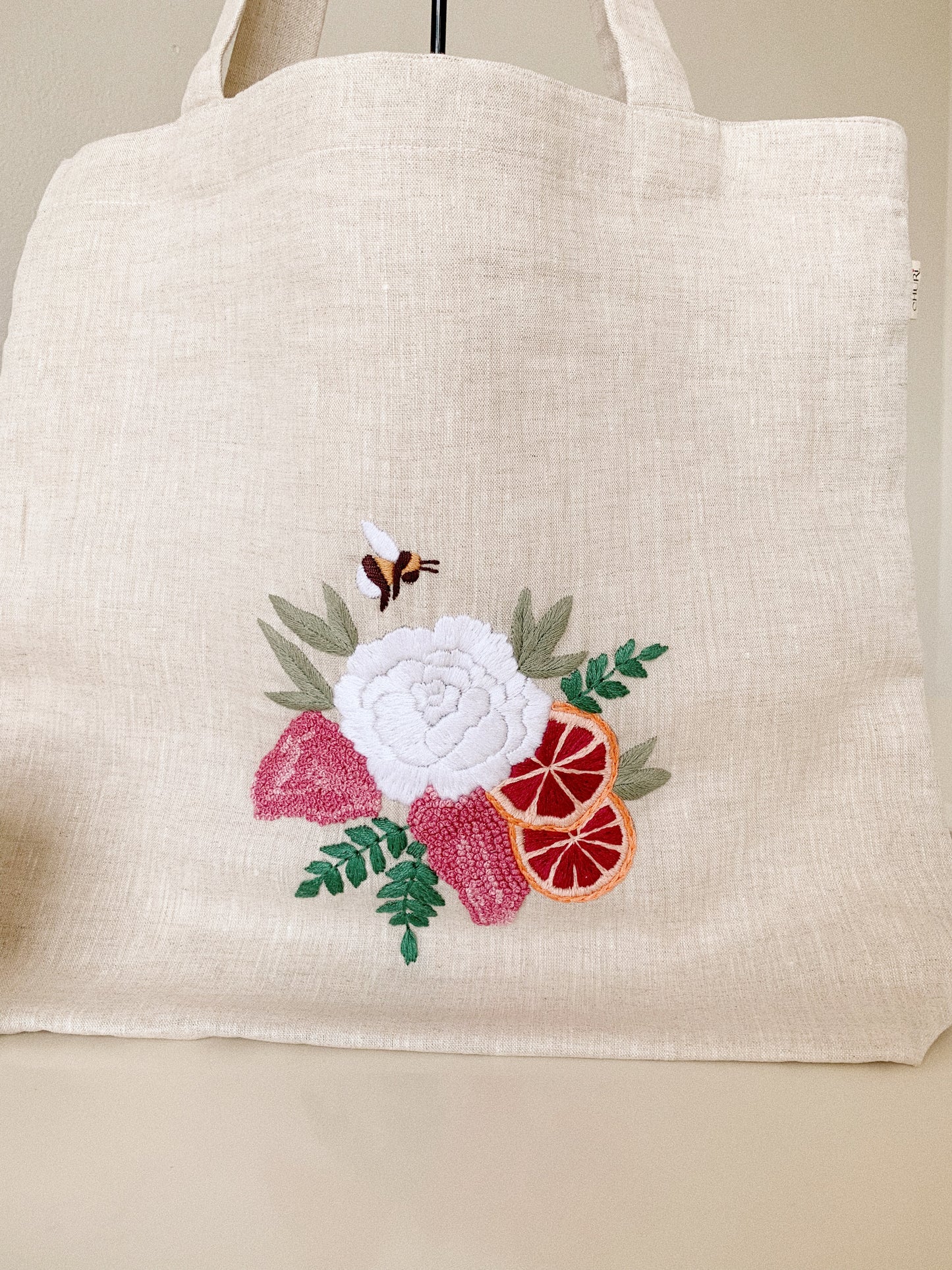Hand embroidered linen tote bag with bee above a flower embroidery.