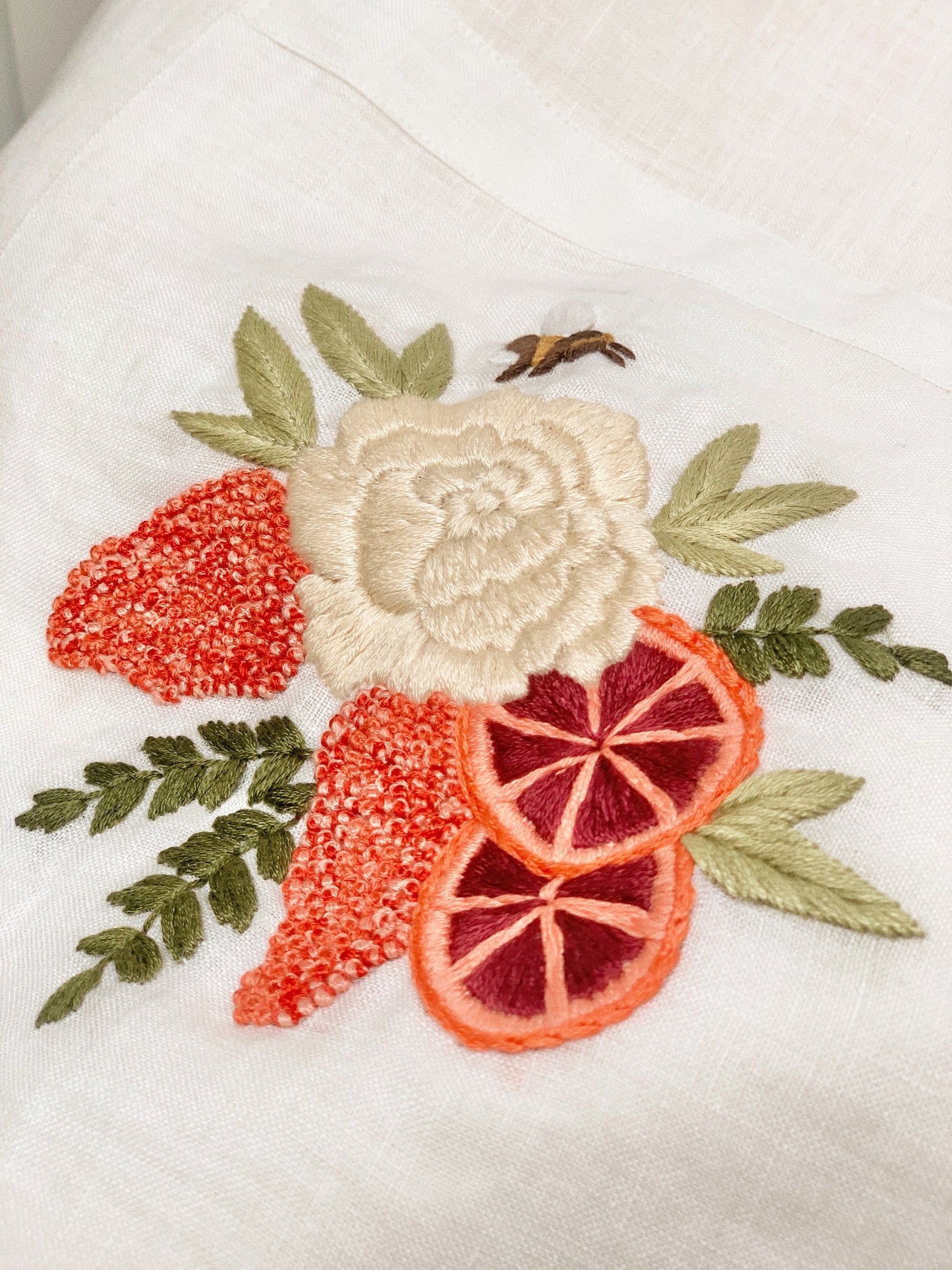 Hand embroidered linen tote bag with bee above a flower embroidery.