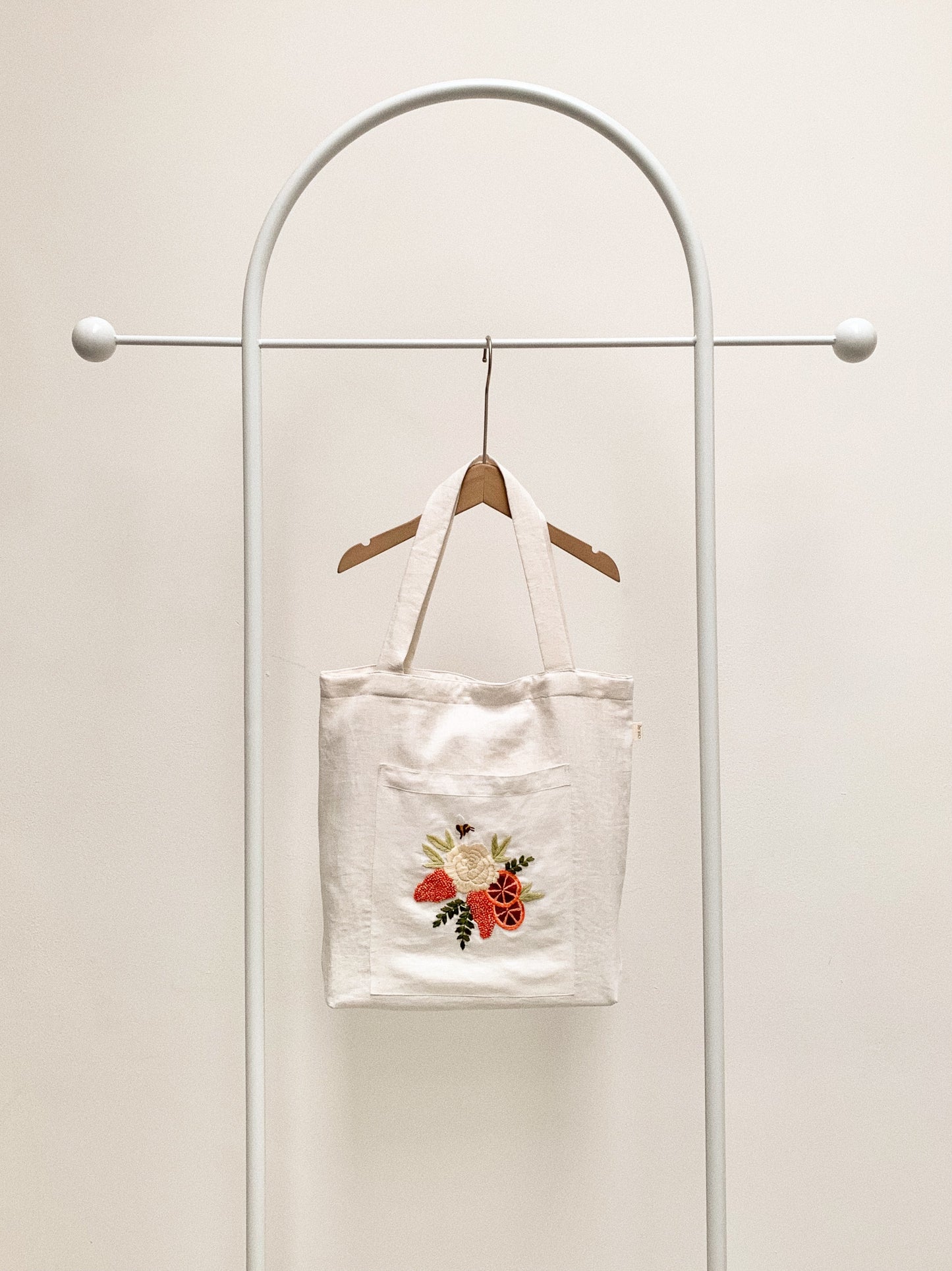 Hand embroidered linen tote bag with bee above a flower embroidery.
