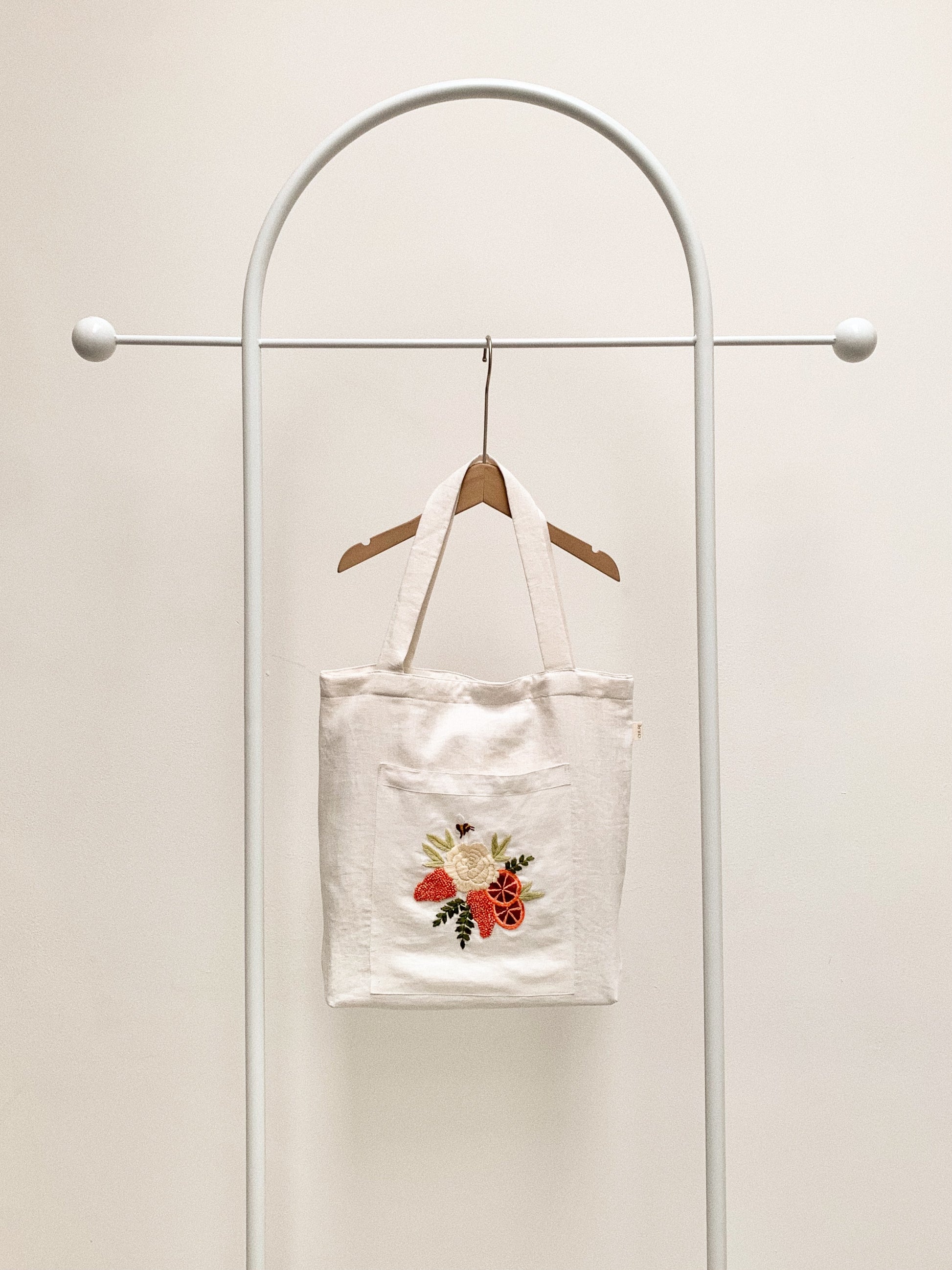 Hand embroidered linen tote bag with bee above a flower embroidery.