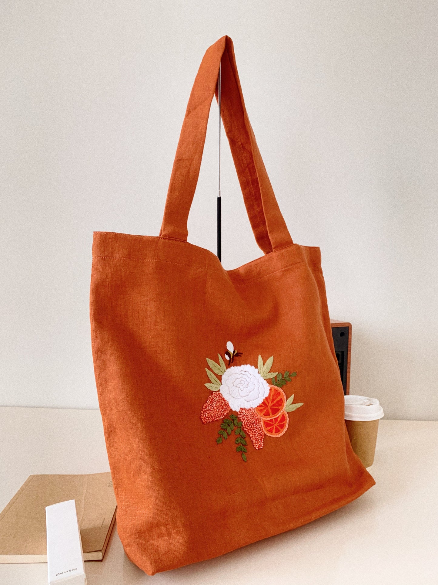 Hand embroidered linen tote bag with bee above a flower embroidery.