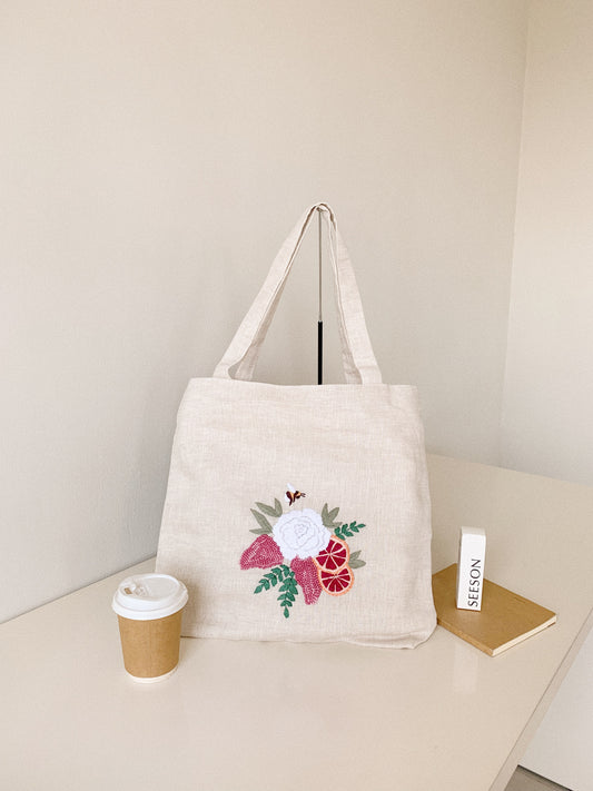 Hand embroidered linen tote bag with bee above a flower embroidery.