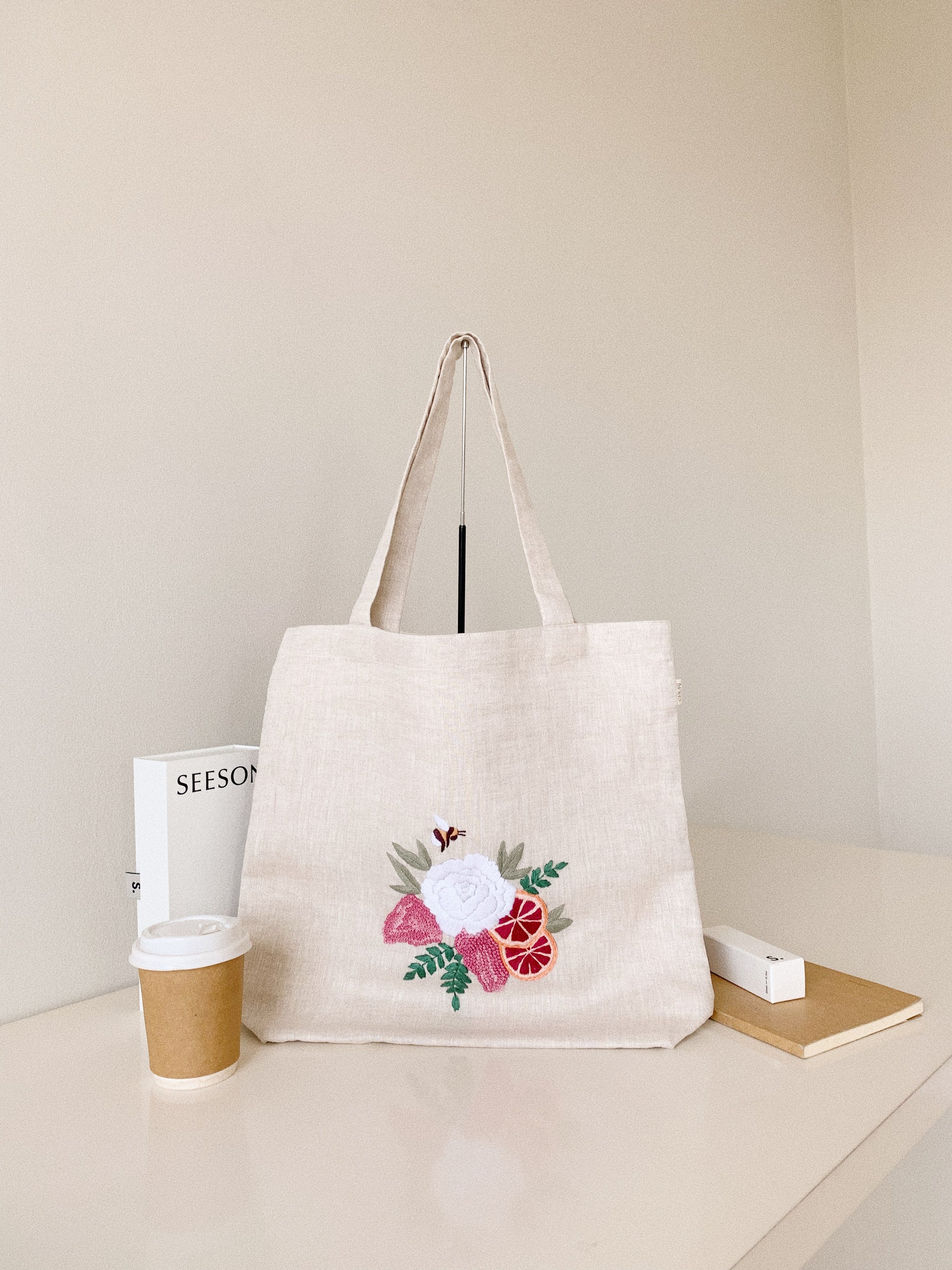 Hand embroidered linen tote bag with bee above a flower embroidery.
